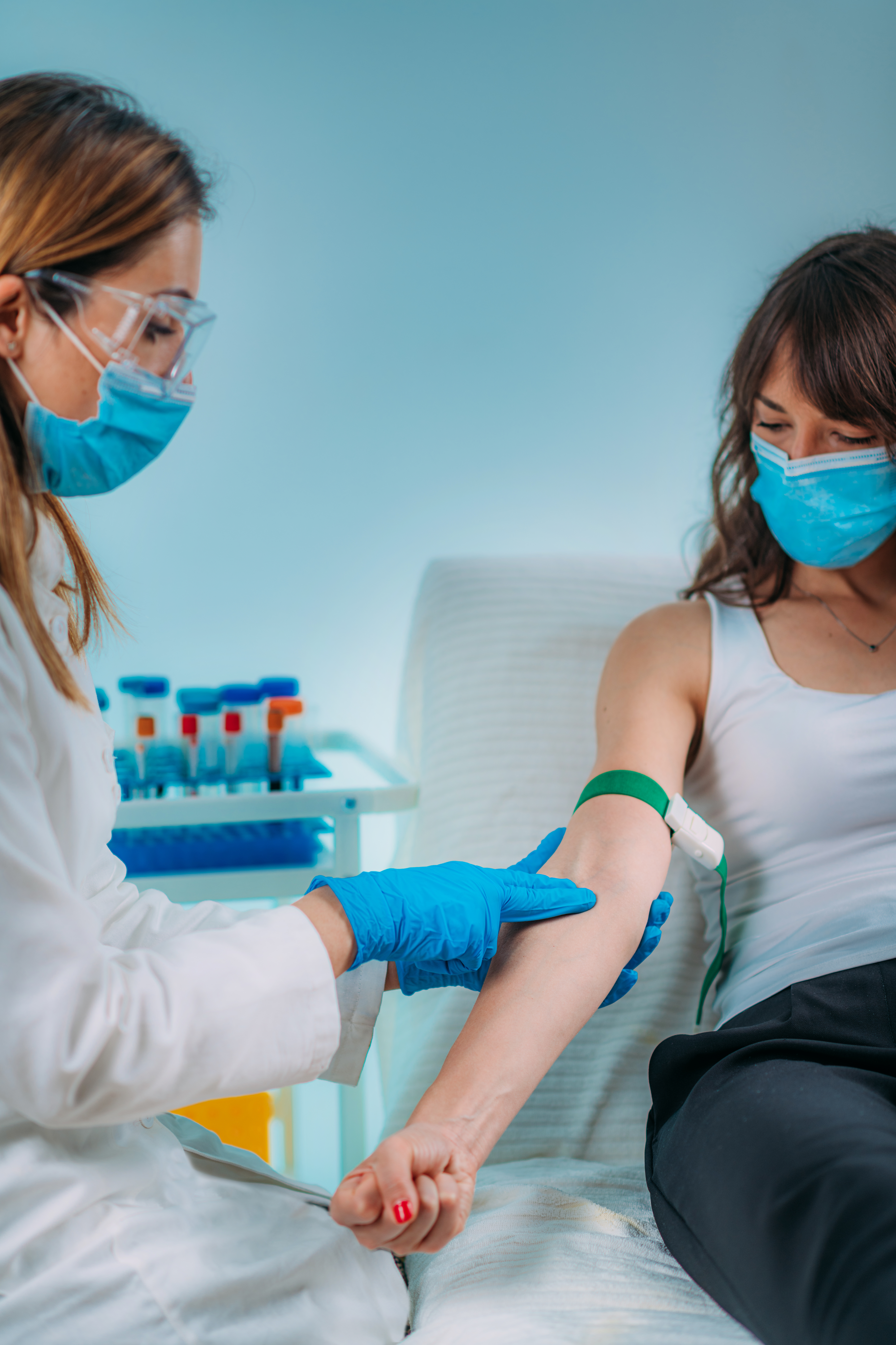 Preparation for phlebotomy procedure, female patient and medical nurse wearing protective masks